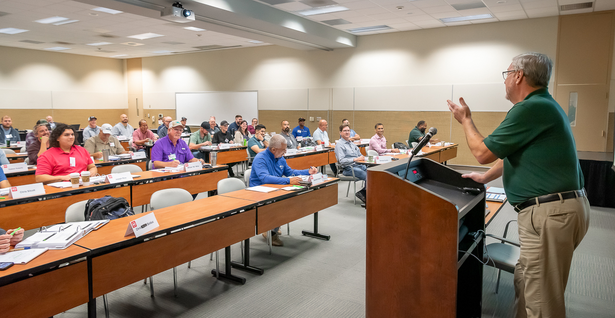 a man speaks at a lectern to a classroom of lifelong learners